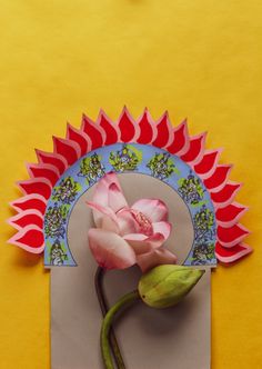 a pink flower sitting on top of a piece of paper next to a yellow wall