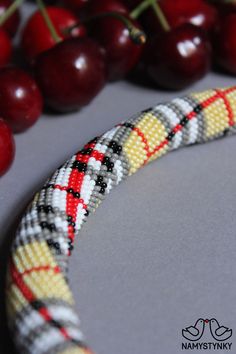 a close up of a beaded bracelet with cherries on the table behind it