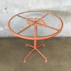 an orange metal table with glass top sitting on concrete flooring next to a wall