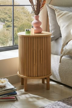 a wooden table with a vase on top of it next to pillows and a window