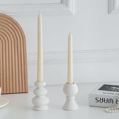 two white candles sitting on top of a table next to a book