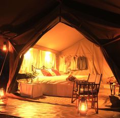 a bed sitting inside of a tent next to two tables with candles on top of it