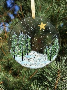 a christmas ornament hanging from a tree with snow and trees in the background