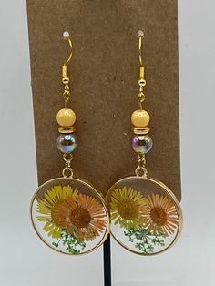 Handmade Earrings - Sunflowers Series Each piece is meticulously handcrafted using craft wire, hypoallergenic earring hooks, and premium beads including crystal, glass, wood, ceramic, acrylic, resin, stone, and silicone beads. Care Instructions: Avoid moisture. Remove prior to bathing, showering, swimming, or exercising. Avoid allowing the item to fold when storing.  Shipping Information: Your items will be shipped within 1-2 business days once payment is received. Shipping within the US is via first class mail or you may choose to upgrade to Priority Mail for a small fee. First class shipping is free for orders over $35. Each item is carefully wrapped and packaged for safety during transit. Returns & Exchanges: As this is a wearable item, I do not accept returns or exchanges on this item. Handmade Resin Flower Shaped Earrings, Handmade Resin Flower-shaped Earrings, Resin Dangle Flower Earrings With Ear Wire, Dangle Flower Earrings With Resin And Ear Wire, Dangle Flower Earrings With Ear Wire In Resin, Handmade Round Resin Flower Earrings, Resin Round Birth Flower Earrings, Round Resin Birth Flower Earrings, Resin Flower Charm Dangle Earrings