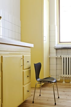 a yellow kitchen with a black chair in front of the stove and cupboards next to it