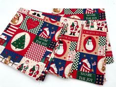 two christmas themed napkins with santa and snowman designs on red, green, white and blue fabric