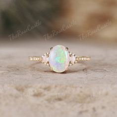 a white opal and diamond ring sitting on top of a stone surface with the words,