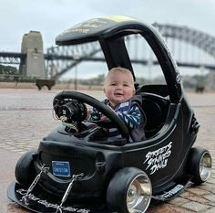 a small child in a toy car with a bridge in the backgroung