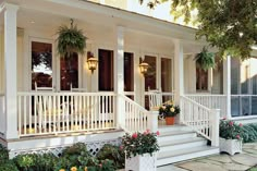 the front porch of a house with potted plants on the steps and flowers hanging from the balconies