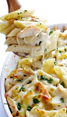 a wooden spoon scooping pasta from a casserole dish with chicken and parmesan cheese