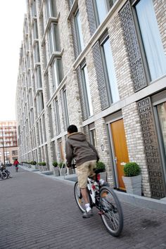 a man riding a bike down a brick street next to tall buildings and potted plants