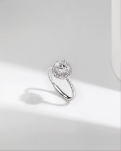 a diamond ring on a white surface with light coming in from behind it and the center stone is surrounded by small round diamonds