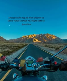 a motorcycle driving down the middle of a road with mountains in the backgroud