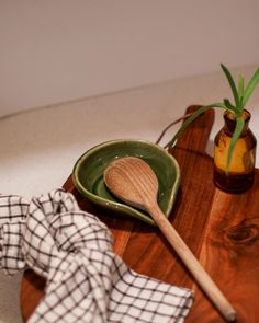 a wooden spoon sitting on top of a green plate next to a bottle and napkin