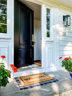 a black front door with two potted red flowers on the side and a welcome mat