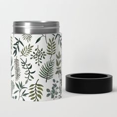 a white can with green leaves on it sitting next to a black lid and thermos