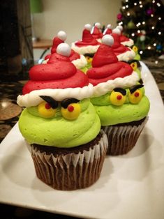 two cupcakes with green frosting and santa hats on them sitting on a plate