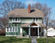 a green house with white trim on the front and side of it, surrounded by trees