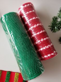 two rolls of green and red christmas wrapping on top of a white table next to evergreen branches