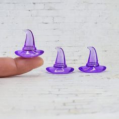 three purple plastic gnomes sitting in front of a white brick wall with one hand holding the top