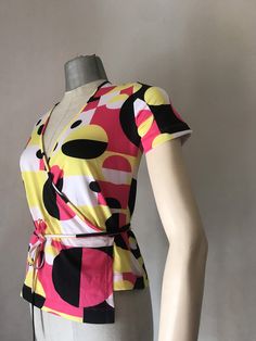 "90s Vintage does 70s stretchy double breasted top that features a very cool, geometric squared and circles pattern Shocking pink and bright yellow mixed with black and white makes it so groovy and some may say rave? It ties with a long cord all around the waist. It was then, in the early 90s that the super stylish dance band \"Deee Lite\" brought back that psychedelic style in fashion. (All the credits to the band!) ‼️Be aware - only one piece is available----- 🌀MEASUREMENTS: (taken while layi Chic Spring Tops With Geometric Pattern, Fitted Summer Tops With Retro Print, Trendy Stretchy Colorful Tops, Bold Graphic Print Tops For Spring, Patterned Fitted Short Sleeve Tops, Bold Vibrant Print Tops For Spring, Fitted Tops With Bold Print For Summer, Fitted Patterned Short Sleeve Tops, Fitted Patterned Top With Short Sleeves