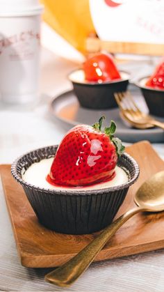 a strawberry on top of yogurt in a bowl with gold spoons next to it