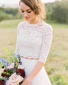 a woman in a white dress holding a bouquet of flowers and wearing a lace crop top