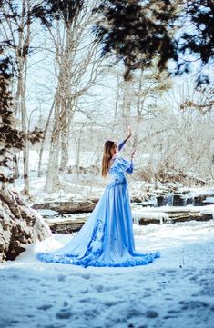 a woman in a blue dress is standing in the snow with her arms raised up