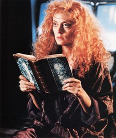 a woman with long red hair is holding a book and looking at the camera while sitting down