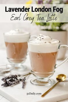 two cups filled with liquid sitting on top of a white table next to spoons