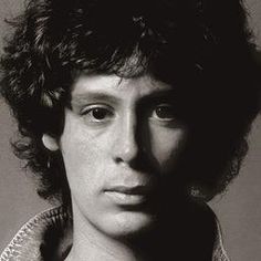 a black and white photo of a young man with curly hair wearing a sweater looking at the camera