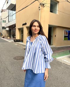 a woman standing in the middle of an empty street wearing a blue and white striped shirt