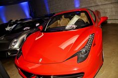 a red sports car is parked in a garage with other cars behind it on display