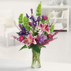 a vase filled with lots of purple and pink flowers on top of a white table