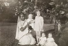 an old black and white photo shows two women holding babies in front of a tree