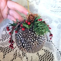 a person is holding a vase with flowers and pine cones in it on a table