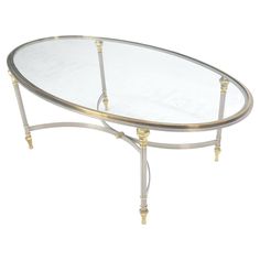 an oval glass table with gold trimmings on the legs and a metal frame