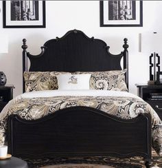 a bed with black headboard and foot board in a white walled room, surrounded by pictures on the wall