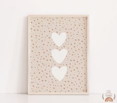 three hearts cut out of paper in a white frame against a wall with polka dots