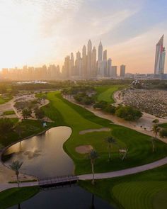 an aerial view of a golf course with the city skyline in the background at sunset