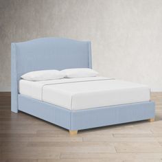 a blue bed with white pillows on top of it and wooden flooring in front of the headboard