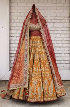 an orange and gold lehenga on display in front of a white brick wall