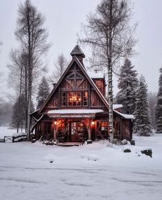 a cabin in the woods with snow on the ground and lights shining from the windows