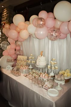 a table topped with lots of pink and white balloons next to a cake covered in cupcakes