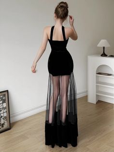 a woman in a black dress standing on a hard wood floor with her back to the camera