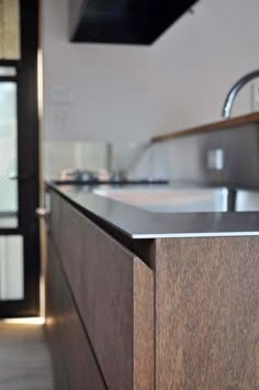 a modern kitchen with stainless steel appliances and wood cabinetry in the foreground, along with an open door leading to another room