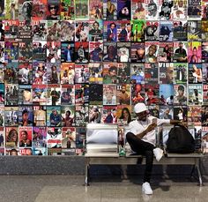 a man sitting on a bench in front of a wall covered with posters