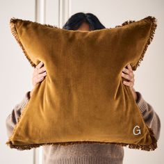 a woman holding a brown pillow with the letter g on it