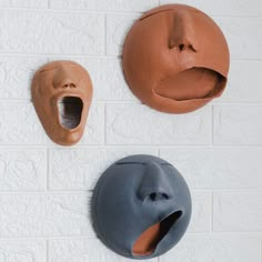 two clay masks are hanging on the wall, one has its mouth open and another has it's tongue out