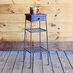 a small table with a cup on it sitting on a wooden floor next to a wall